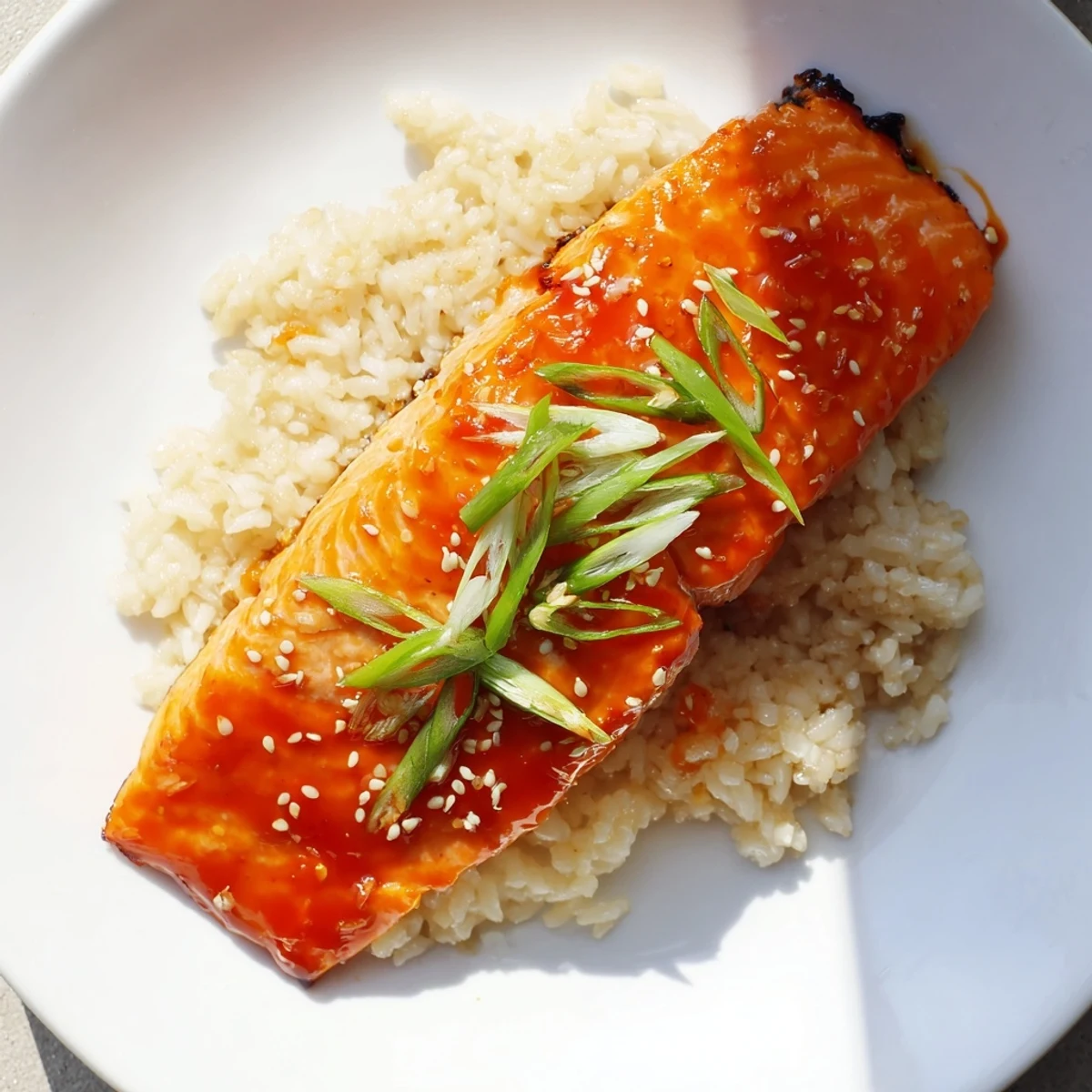 Close view of pan-seared Sticky Orange Salmon, glistening with sauce beside fluffy white rice.
