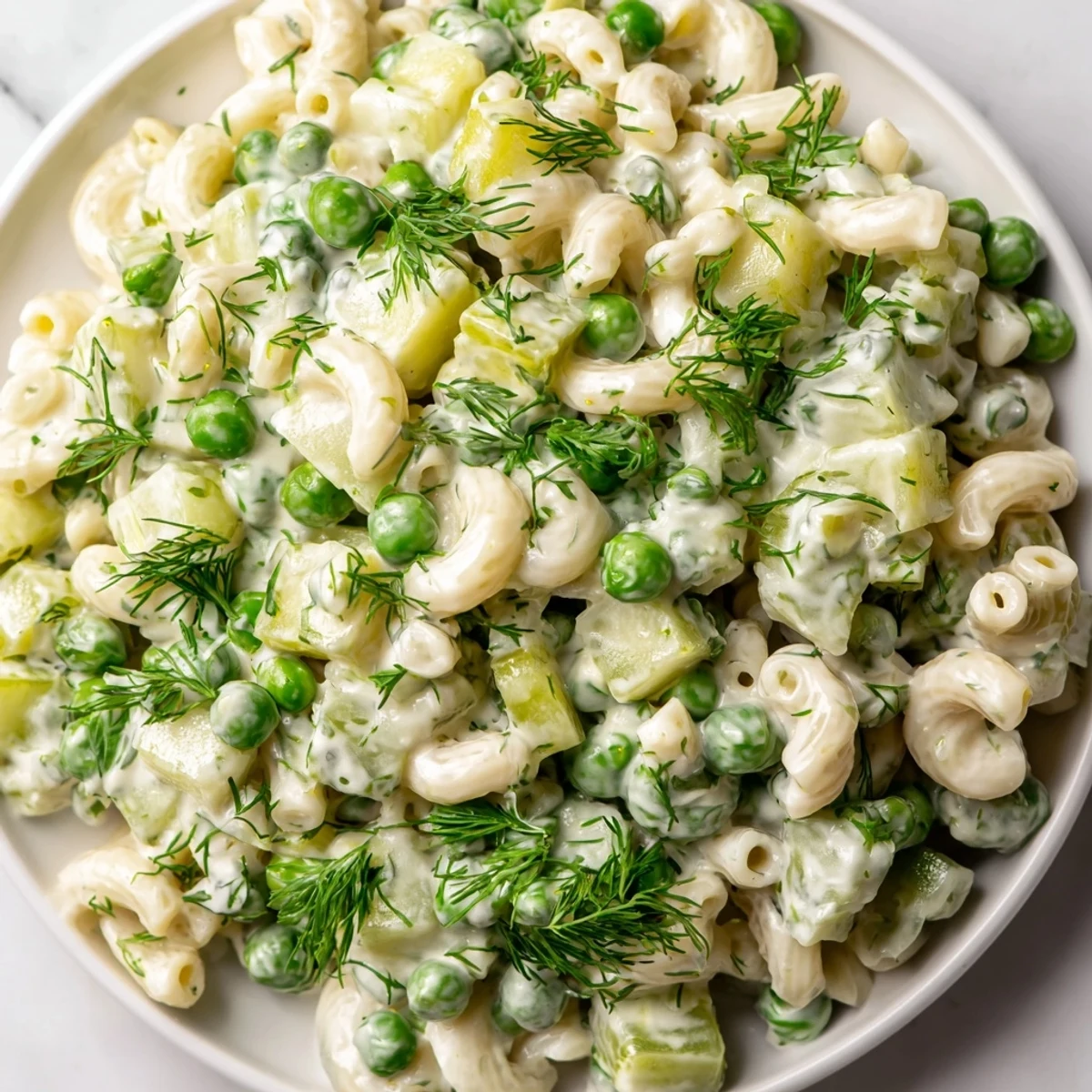 A vibrant bowl of Creamy Dill Pickle Pasta Salad, featuring ditalini, bright green peas, and crunchy diced pickles in a rich, tangy dressing.  