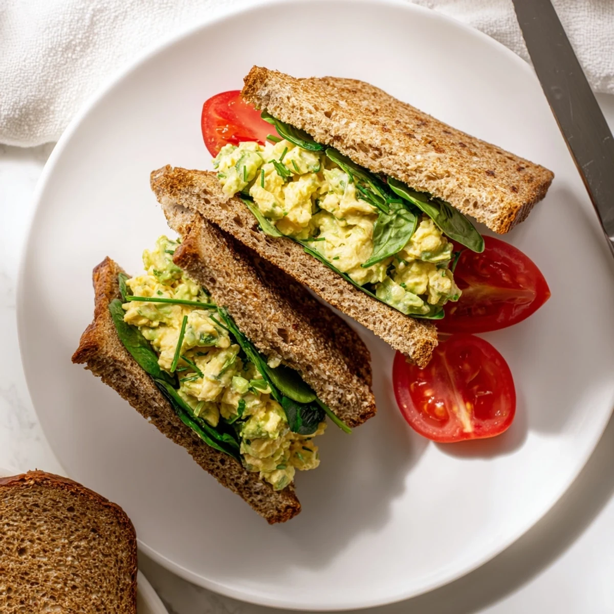 Two halves of a homemade Avocado Egg Salad Sandwich stacked on a napkin, ready to serve for a quick vegetarian meal.
