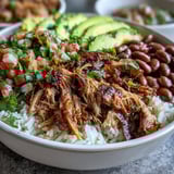 A steaming Carnitas Bowl topped with fresh pico de gallo, chopped cilantro, and lime wedges.