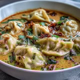 Quick coconut curry soup with dumplings, featuring colorful vegetables and a spicy chili oil drizzle. 