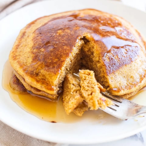 A stack of fluffy pumpkin spice pancakes topped with maple syrup and whipped cream, perfect for a cozy autumn breakfast.