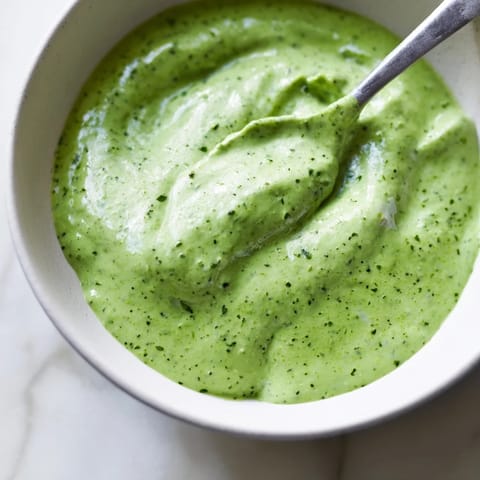 Freshly blended Green Goddess Dressing in a glass jar with chopped herbs, ready for dipping.