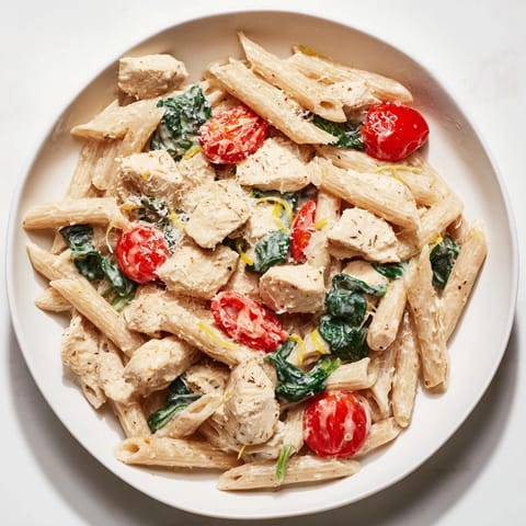 A close-up of Greek Yogurt Chicken Pasta, garnished with fresh basil and Parmesan, highlighting the creamy texture and juicy tomatoes.  