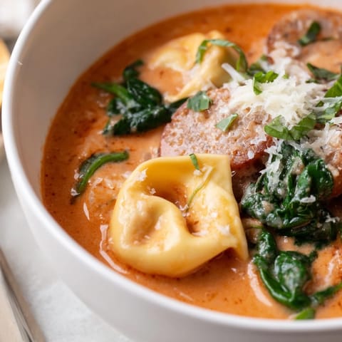 A cozy Tuscan Tortellini Soup ladle full of rich tomato cream, tender pasta, and savory sausage, garnished with Parmesan.