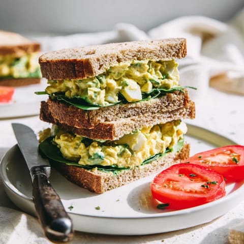 Open-faced Avocado Egg Salad Sandwich on a rustic plate, topped with fresh spinach and ripe tomato slices for a healthy lunch.
