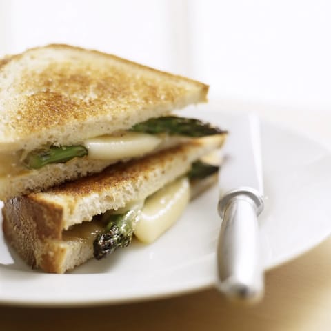 Savory Asparagus & Brie Grilled Cheese sandwich resting on a wooden board, ready to serve with a side salad.