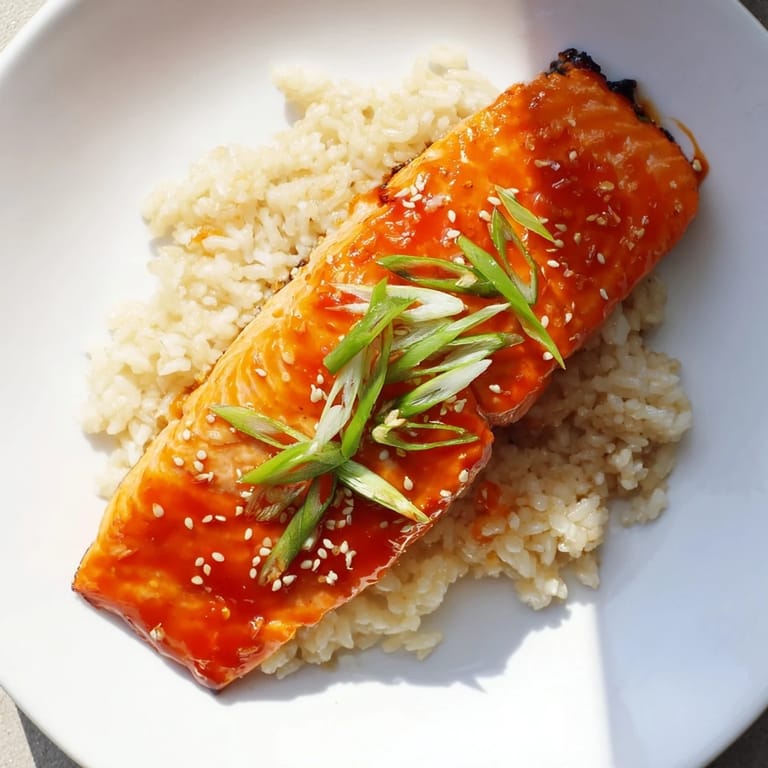 Close view of pan-seared Sticky Orange Salmon, glistening with sauce beside fluffy white rice.